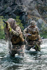 Vertical photo of a two mercenary soldiers ford a river during a sabotage operation.