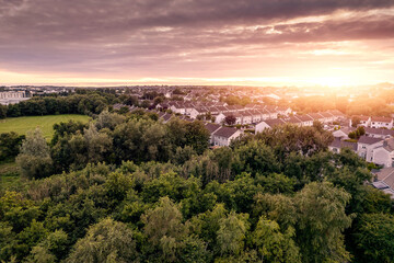 Aerial view on high dense residential area at sunset. House estate by a small park with green trees and fields. Modern family houses with car park and backyard. Galway, Ireland.