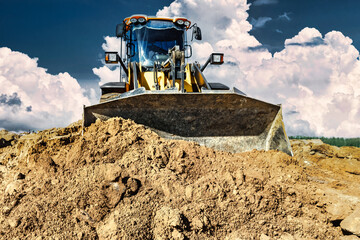 Powerful bulldozer or loader moves the earth at the construction site against the sky. An...