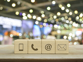 Mobile phone, telephone, email address, mail icon on wood block cubes on wooden table over blur light and shadow of shopping mall, Business customer service and support online concept