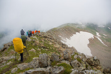 A group of tourists walks along a mountain range in the fog.