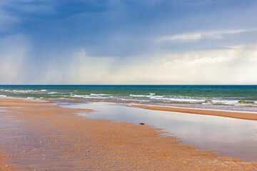 Fototapeta na wymiar Seascape view at a sand beach with rain in the horizon