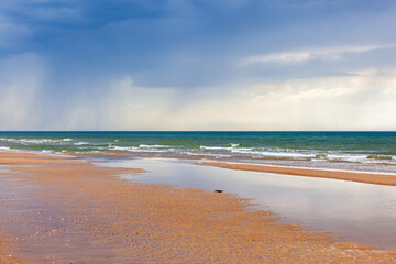 Seascape view at a sand beach with rain in the horizon