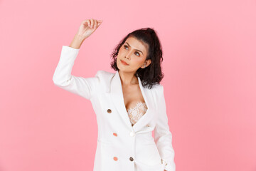 Portrait studio shot of Asian sexy curly hairstyle professional successful businesswoman in white fashionable casual suit with lace lingerie crop top bra standing look at camera on pink background