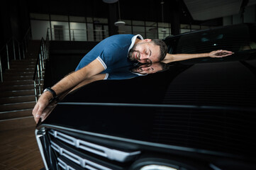 Fototapeta premium Happy caucasian man hugging the hood of his new car in a car dealership.