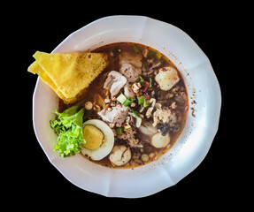 Isolated Tom Yum Pork Noodles with Egg in a white bowl on a black background. Thai food.