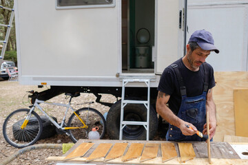 white caucasian man painting wood for the interior of his motor home. Mobile home repair.