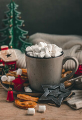 Coffee or cocoa with marshmallows in a ceramic mug, wooden Christmas toys and decorations, sweets on a dark background. Cozy composition with Christmas decor