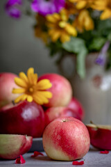 A bright bouquet of flowers in a ceramic vase and red ripe apples. Stylish and cozy autumn still life with fruit