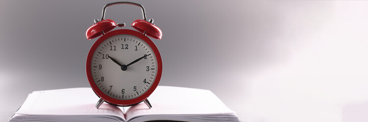 Red retro clock stand on top of open notebook or book