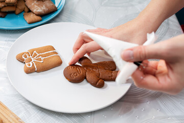 A female's hands decorates gingerbread with icing sugar. Close-up of cookies on plate. Top view. The concept of Christmas cooking