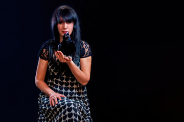 A beautiful brunette woman with a crow sitting on the hand on black background.