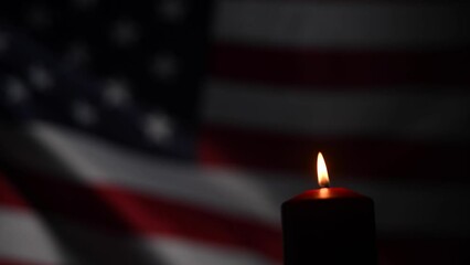 Burning candle against the background of the waving flag of the united states of america in the dark.