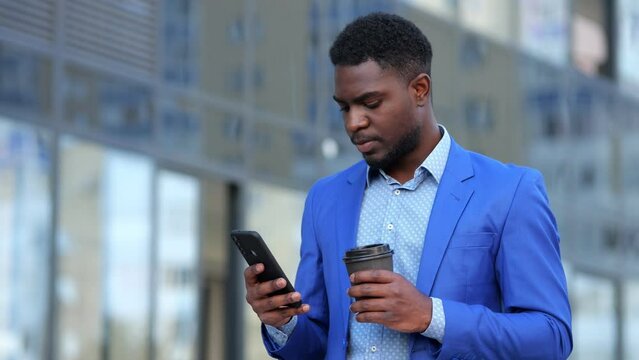 African American businessman reads important articles about business on smartphone. Mature entrepreneur holding coffee cup takes small break outdoor
