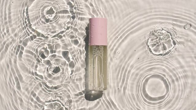 Cosmetic bottle, vial for oil, liquid, collagen serum on water surface with drops. Women's cosmetics skincare. Sample of layout of package beauty product. High quality 4k footage