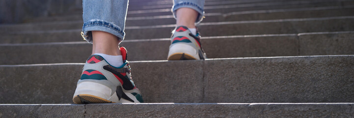 Fototapeta na wymiar Female legs in sports sneakers going up stairs closeup