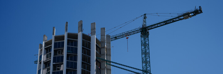 Fototapeta premium Construction crane standing near modern building against blue sky
