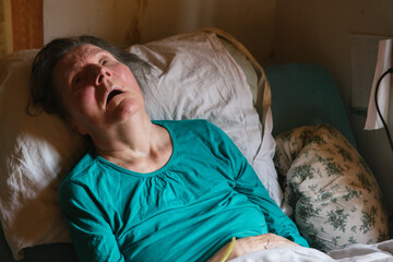 Paralyzed elderly lady lying on bed at home