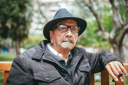 Senior man in hat sitting on bench with cigar