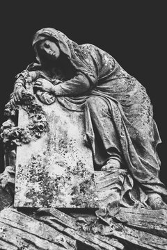 Ancient stone statue of sad and desperate woman on tomb. Copy space. Black and white image.