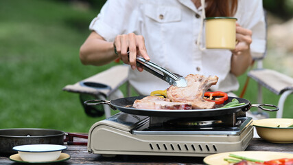 Young woman grilled bbq and preparing food for dinner during camping in nature park on beautiful day