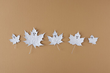 Creative flat lay with autumn leaves painted in white like ghost on beige background. Halloween minimal concept.