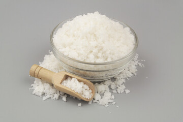 Coarse sea salt in bowl and wooden scoop on gray background.