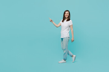 Fototapeta na wymiar Full body side view young caucasian woman 20s wear white t-shirt walking going strolling point index finger aside on workspace area mock up isolated on plain pastel light blue cyan background studio.