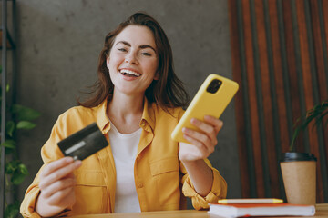 Young smiling employee business woman wear casual shirt using mobile cell phone credit bank card...