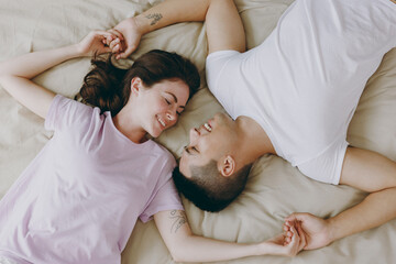 Top view view from above fun lovely young couple two family man woman she he wear t-shirt pajama hold hands lying in bed rest spend time together in bedroom home in own room hotel. Real estate concept