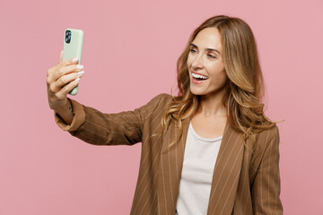 Young successful employee business woman 30s she wearing casual brown classic jacket doing selfie shot on mobile cell phone post photo on social network isolated on plain pastel light pink background.