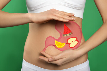 Woman with image of stomach full of food drawn on her belly against green background, closeup....