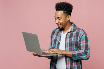 Young smiling happy man of African American ethnicity 20s he in blue shirt hold use work on laptop pc computer isolated on plain pastel light pink background studio portrait People lifestyle concept