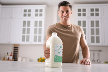 Man with gallon bottle of vegan milk at white marble table in kitchen