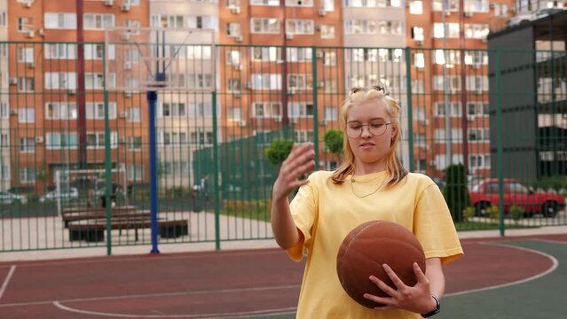 A teenage girl with a basketball in her hands on the court in the courtyard.