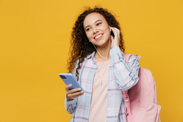 Young minded black teen girl student she wear casual clothes earphones backpack bag mobile cell phone listen to music isolated on plain yellow color background High school university college concept.