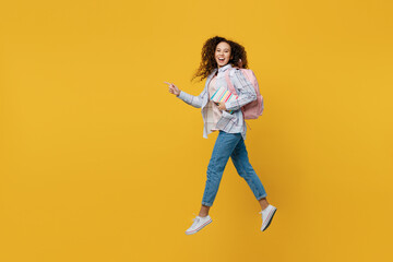 Full body young black teen girl student wear casual clothes backpack bag jump high look camera run point finger aside isolated on plain yellow color background. High school university college concept.
