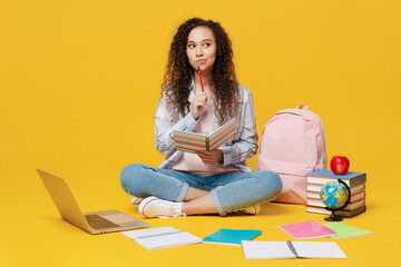 Full body minded young black teen girl student she wearing casual clothes backpack bag hold books sitting on floor isolated on plain yellow color background. High school university college concept