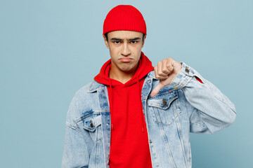 Fototapeta premium Young sad unhappy displeased middle eastern man 20s he wear denim jacket red hat showing thumb down dislike gesture isolated on plain pastel light blue cyan background studio People lifestyle concept
