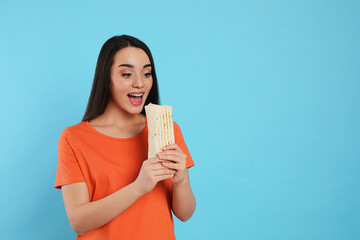 Young woman eating tasty shawarma on turquoise background. Space for text