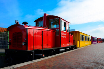 Red Diesel engine and colorful train with narrow gauge coaches of tourist railway on Langeoog island, North Sea Germany. Public transport from port to village on pedestrian vacation destination.