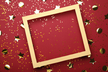 Wooden frame and confetti on red background, flat lay. Space for text