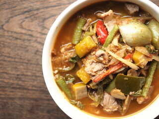 Top view bowl of Kaeng Pa or jungle curry, Thai hot and spicy mixed herb, spices, vegetables, and pork red curry, on wood