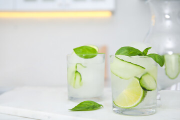 Tasty fresh cucumber water with sliced lime and basil on white table indoors