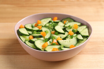 Tasty fresh salad with cucumber in bowl on wooden table, closeup