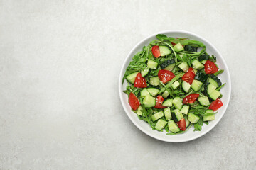 Delicious salad with cucumbers, tomatoes and sesame in bowl on light table, top view. Space for text