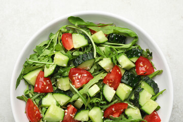 Delicious salad with cucumbers, tomatoes and sesame in bowl on light table, top view