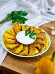 Fried patisson or yellow zucchini with sour cream garlic sauce and greens, on wooden background. Vertical