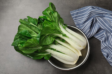 Fresh green pak choy cabbages with water drops in sieve on grey table, top view - obrazy, fototapety, plakaty
