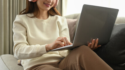 Happy young woman wearing headphone surfing internet on laptop in cozy winter or autumn weekend